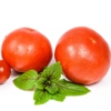 Two tomatoes and a basil leaf on a white surface.